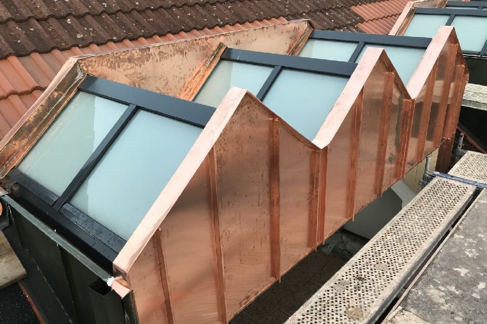 Kupferverkleidete, zickzackförmige Oberlichter auf einem Ziegeldach.