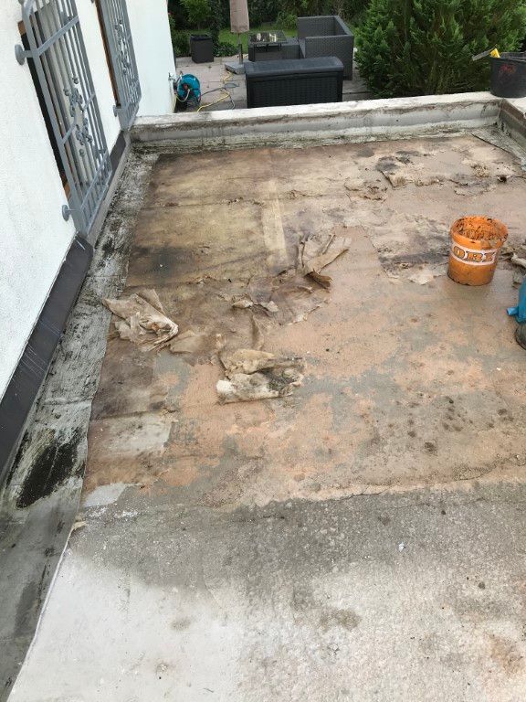 Dach mit abblätterndem Material, Baueimer und Metallgeländer in der Nähe einer weißen Wand.