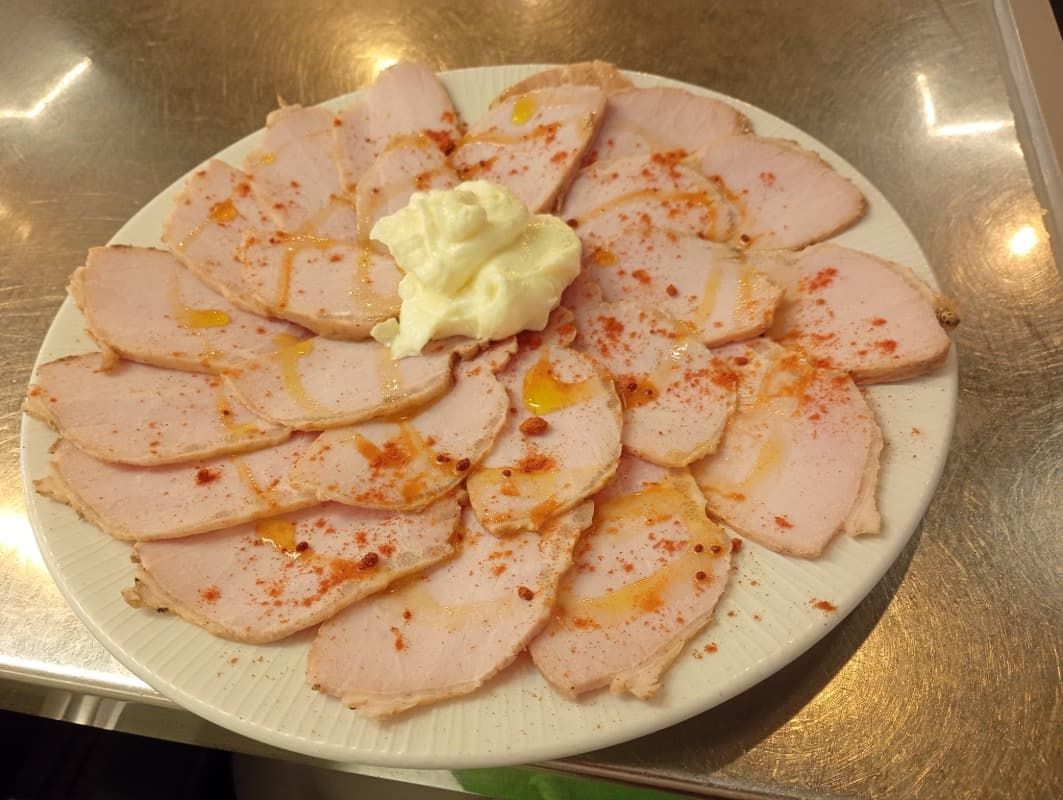 Plato de carne rosada cortada en finas lonchas, cubierta con una cucharada de mantequilla y condimento rojo sobre una mesa.