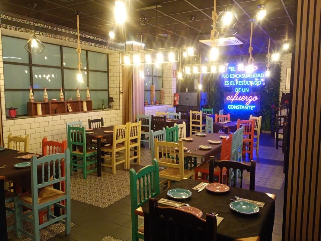 Cafetería interior colorida con sillas de madera, luces colgantes y un escenario iluminado en la parte trasera.