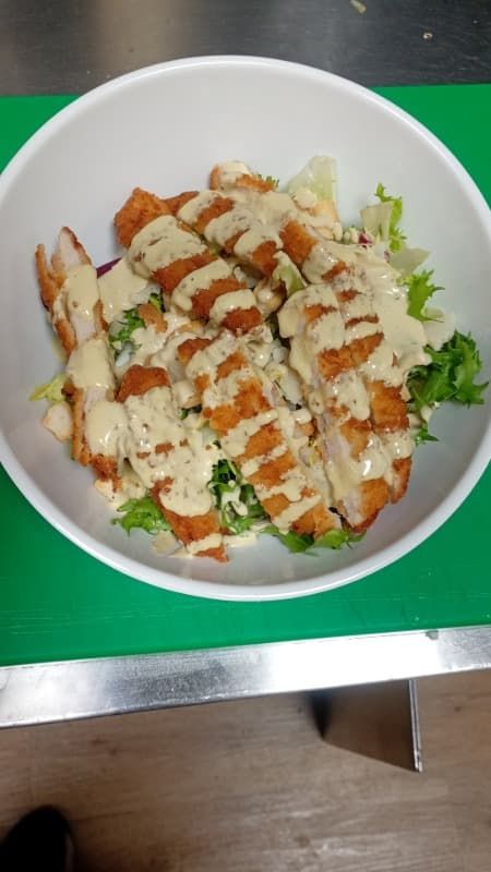 Ensalada blanca con pollo a la parrilla y aderezo cremoso sobre una tabla de cortar verde.