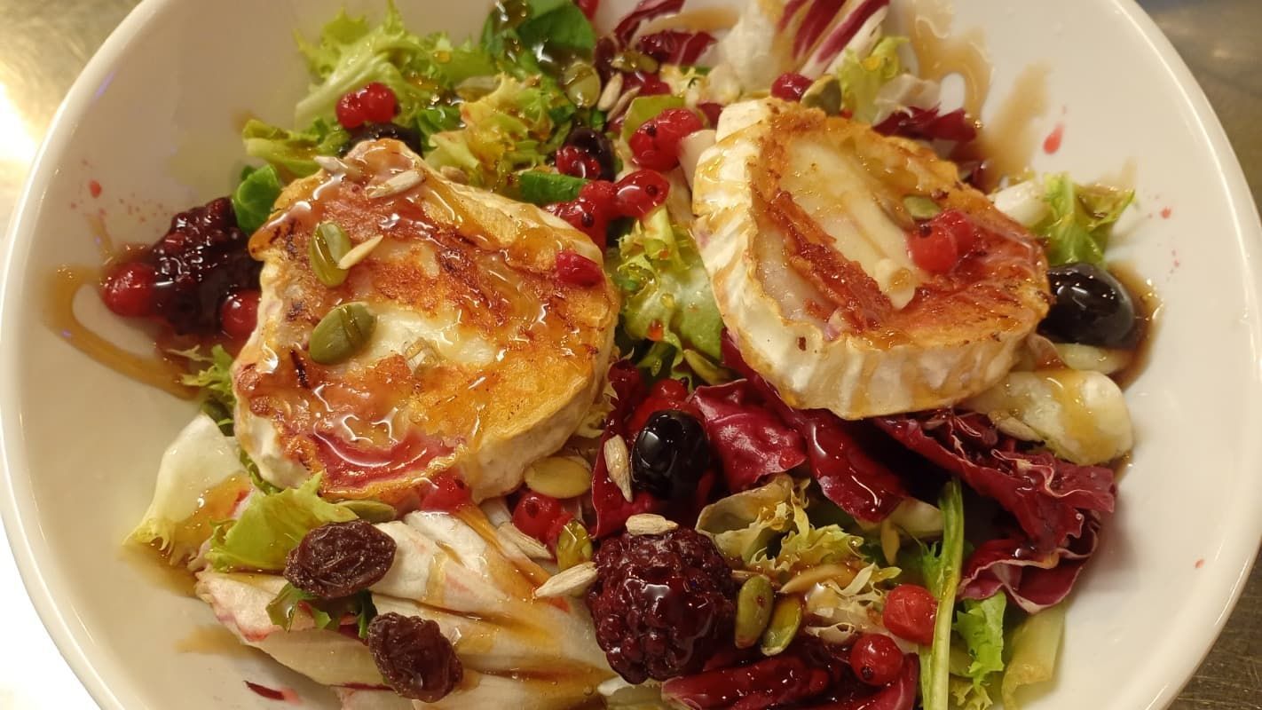 Ensalada con vieiras selladas, verduras y arándanos secos en un tazón blanco.