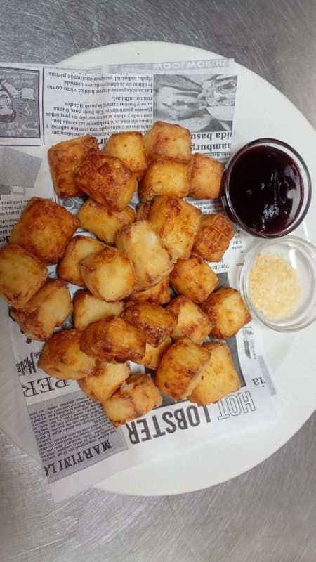 Plato de bocadillos fritos dorados sobre papel de periódico con dos salsas para mojar.
