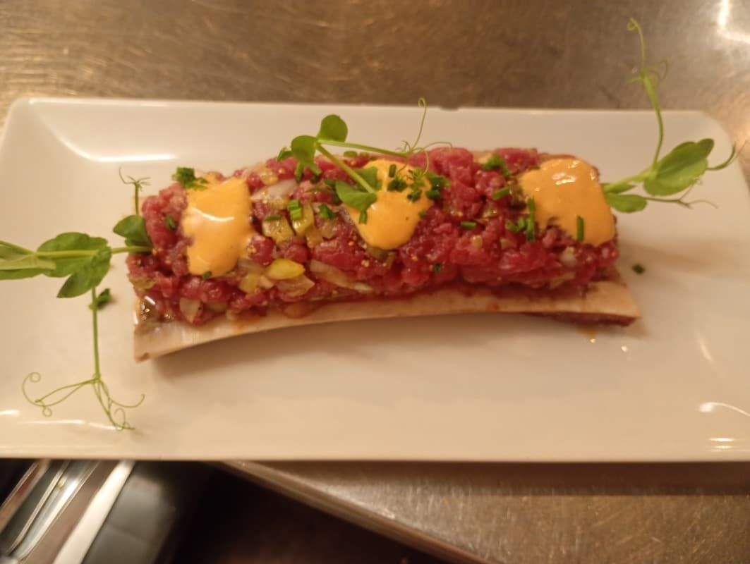 Tartaleta gourmet cubierta con guarnición roja y verde picada y salsa amarilla sobre un plato blanco.