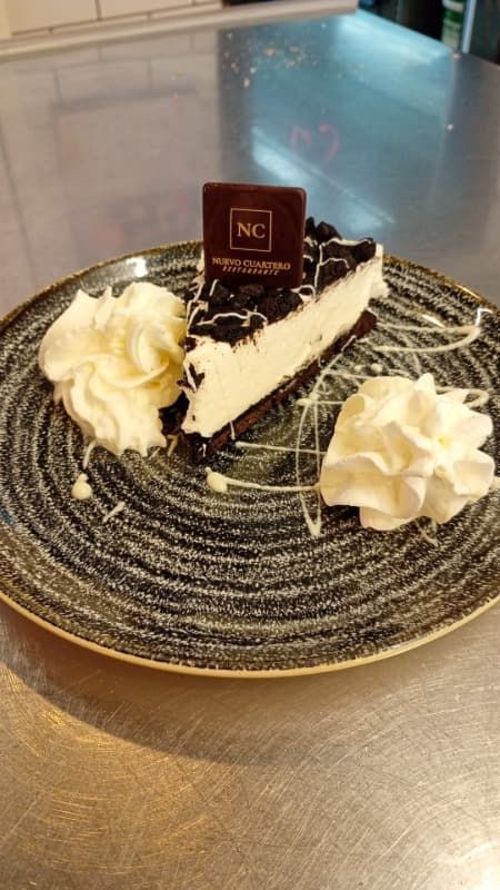Una porción de tarta de queso con chocolate en un plato negro con crema batida y una guarnición de chocolate sobre una encimera.