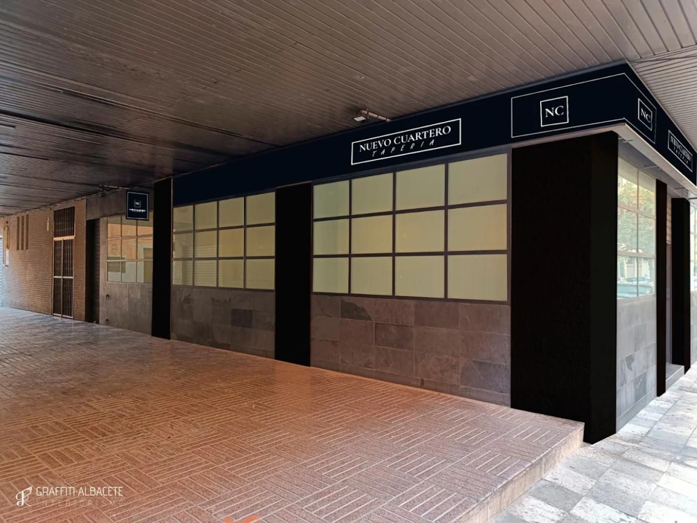 Fachada de tienda con señalización azul oscuro, molduras oscuras y fachada de piedra gris, debajo de una pasarela.