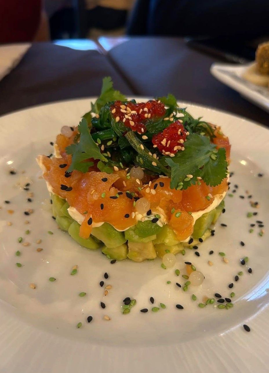 Torre de salmón y aguacate en un plato blanco, adornada con verduras y semillas de sésamo.