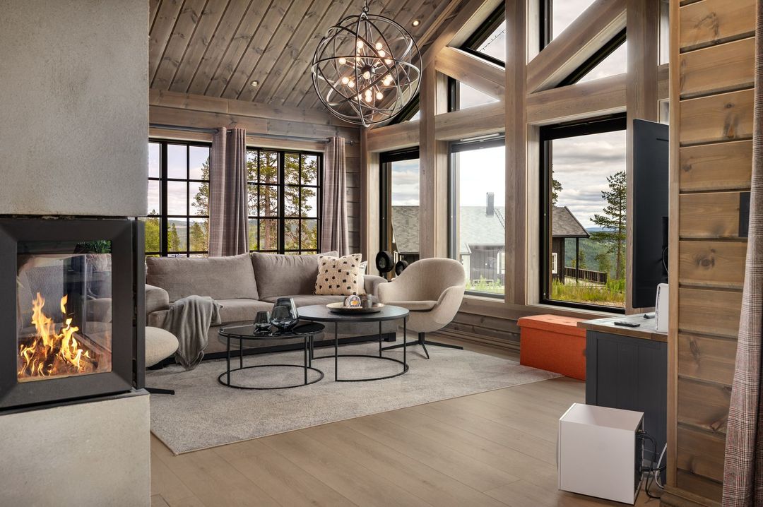 Cozy living room with a fireplace, large windows, and a modern chandelier; neutral tones and wood accents.