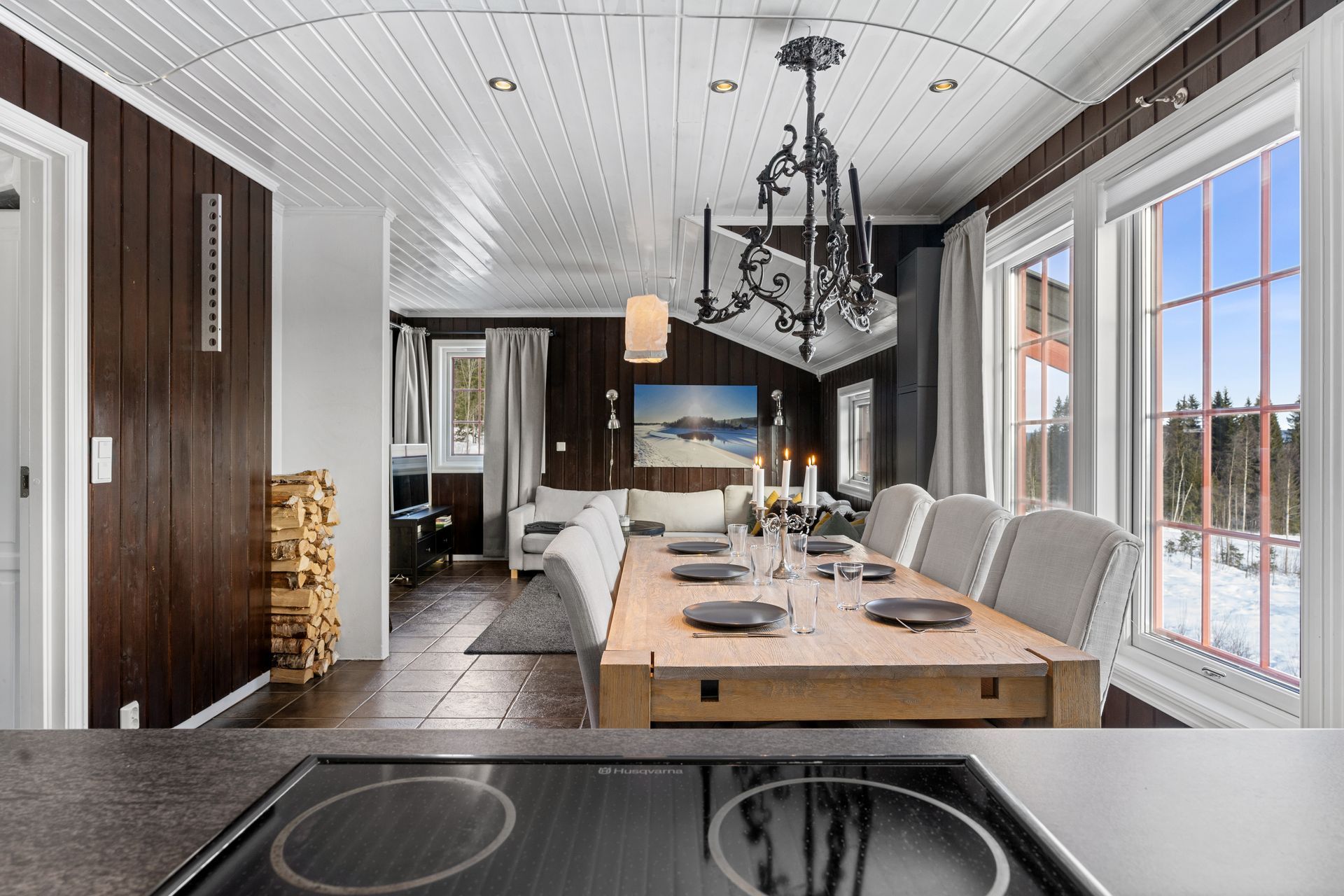 Dining room with a long wooden table, chandelier, and large windows overlooking snow.