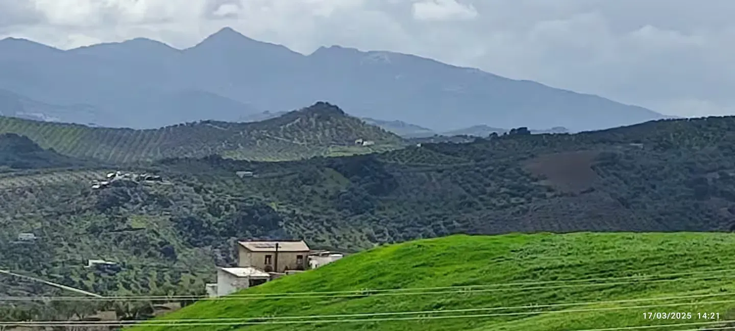 Colinas verdes y montañas a lo lejos, un pequeño edificio se encuentra en el medio, cielo nublado.