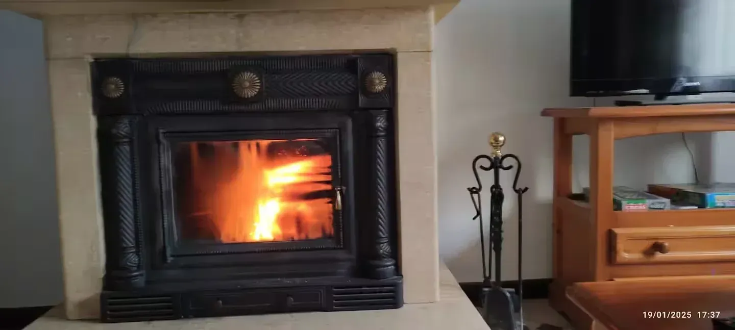 Chimenea con fuego encendido en sala de estar, junto a un televisor y un mueble de madera.