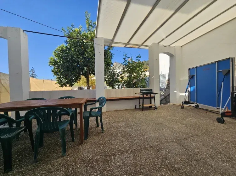 Patio con mesa, sillas, mesa de ping-pong y parrilla bajo un toldo. Día soleado y luminoso.