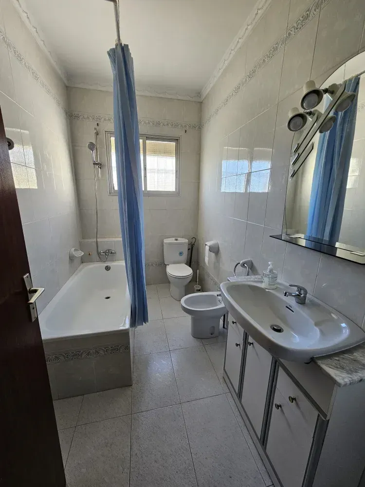 Baño con accesorios blancos, cortina de ducha azul y una bañera larga y blanca.