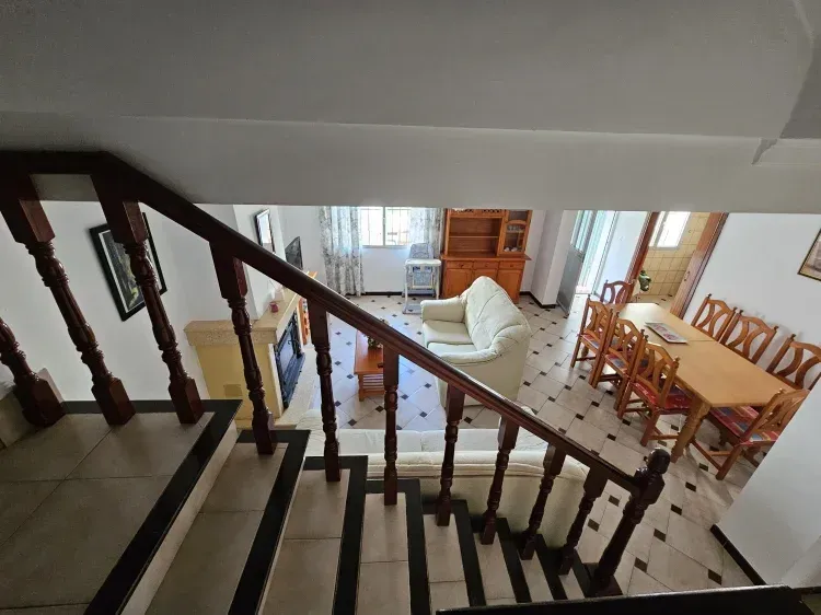 Vista desde las escaleras que dan a una sala de estar con sofá blanco, mesa de comedor y chimenea.