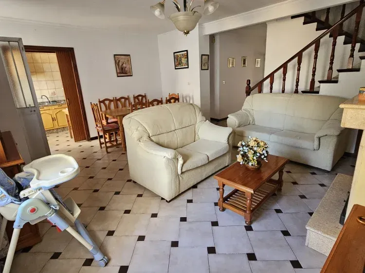 Sala de estar con sofás blancos, mesa de centro de madera, mesa de comedor y escalera.