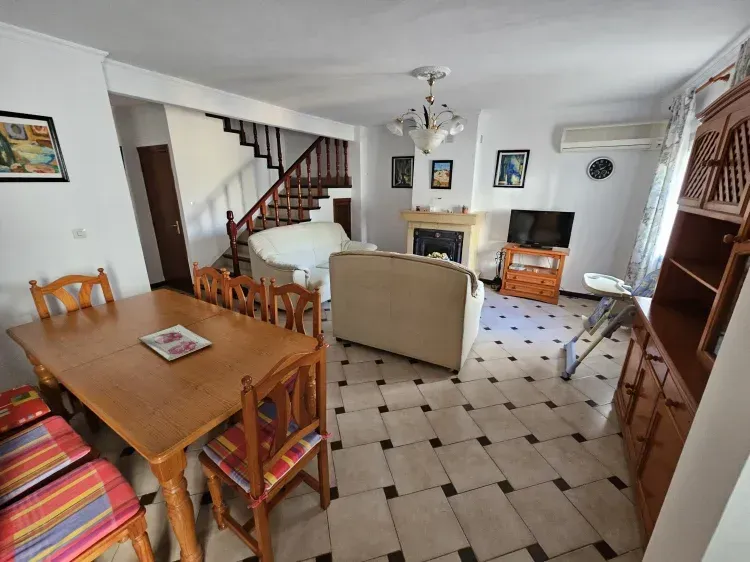 Sala de estar con mesa de comedor, zona de estar, escaleras y chimenea.