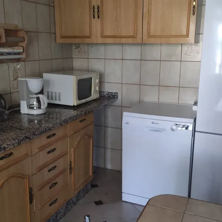 Cocina con gabinetes de madera, encimeras de granito, electrodomésticos que incluyen microondas, lavavajillas y cafetera.