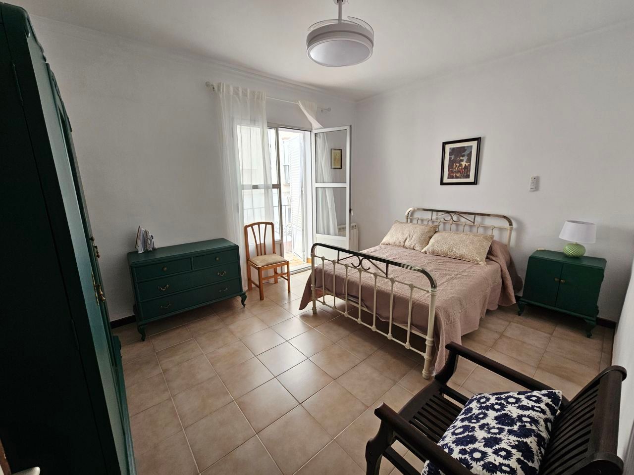 Dormitorio con paredes blancas, cama de hierro, muebles verdes y balcón.