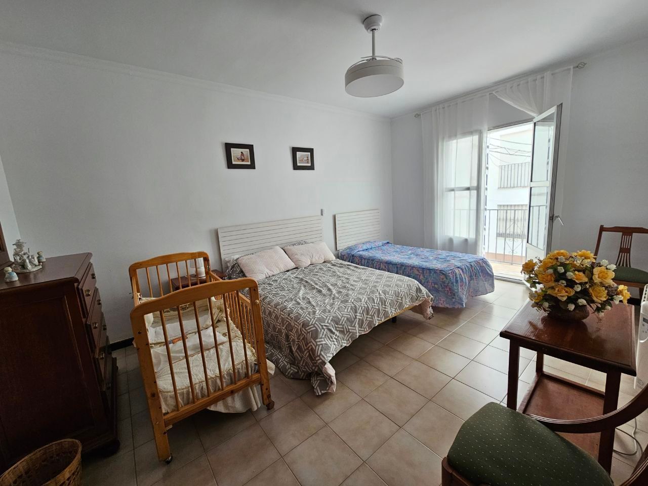 Dormitorio con dos camas, cuna, mesa pequeña y balcón abierto.