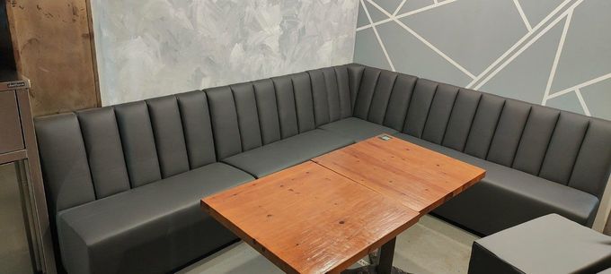Acogedor rincón con un reservado de asientos tapizados en gris y una pequeña mesa de madera en una cafetería o sala de estar.
