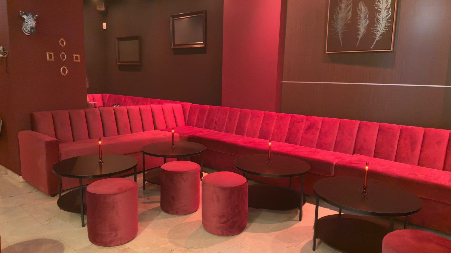 Salón rojo con un banco corrido curvo tapizado en rosa, mesas redondas y taburetes rojos bajo una iluminación tenue.