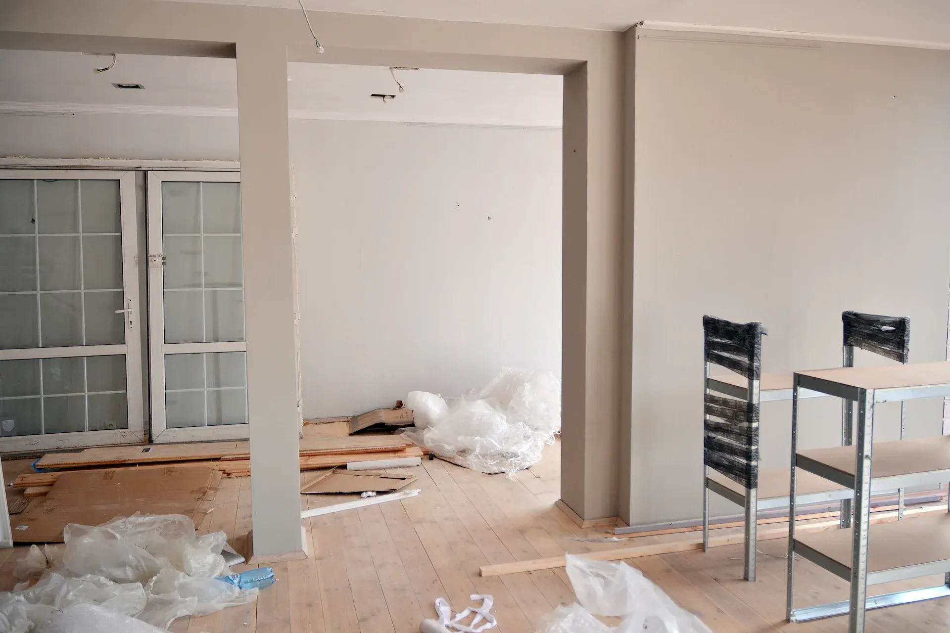 Interior de una habitación en construcción con paredes blancas, pisos sin terminar y materiales de construcción.