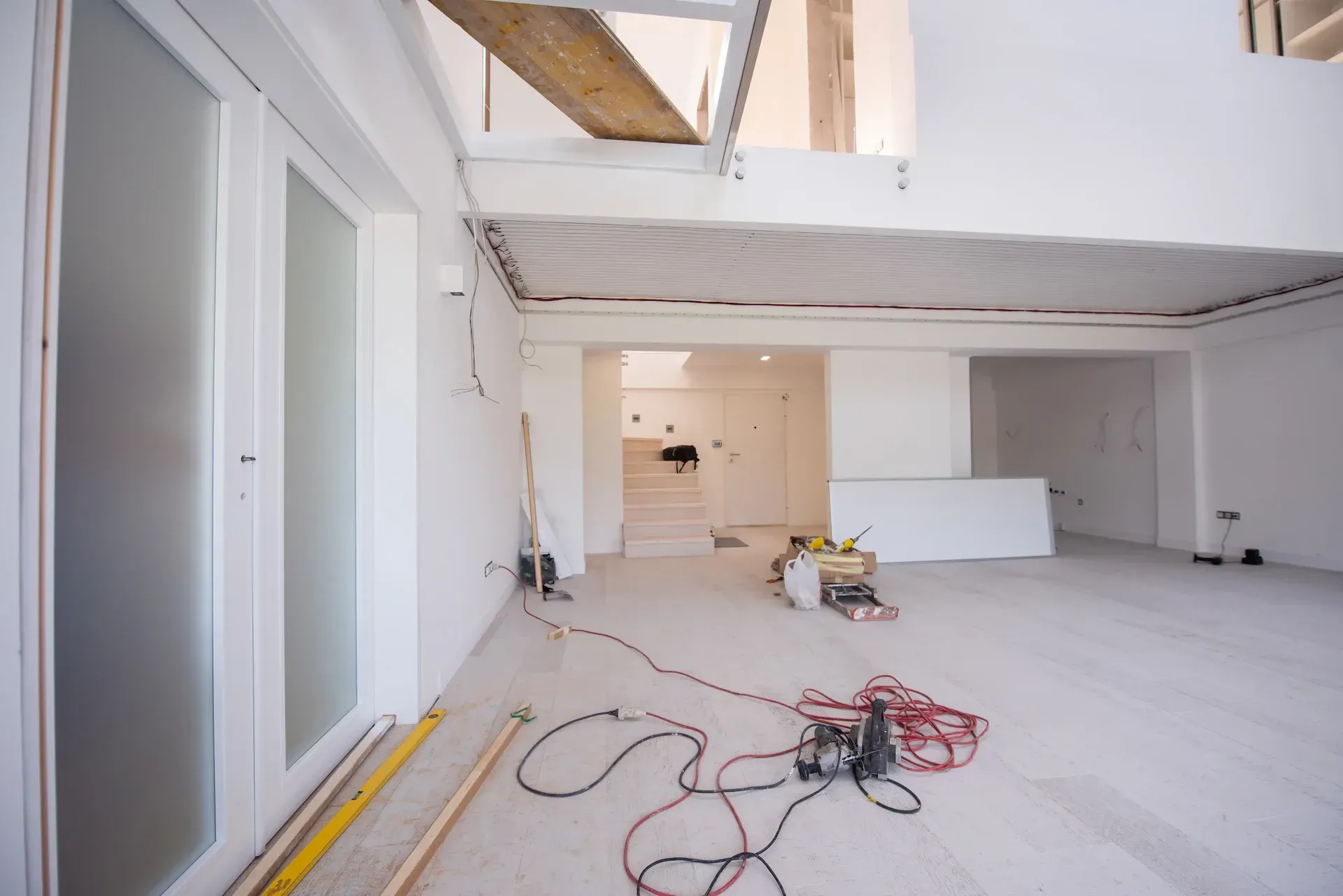 Interior de una habitación en construcción, con paredes blancas, techo sin terminar y herramientas esparcidas en el suelo.