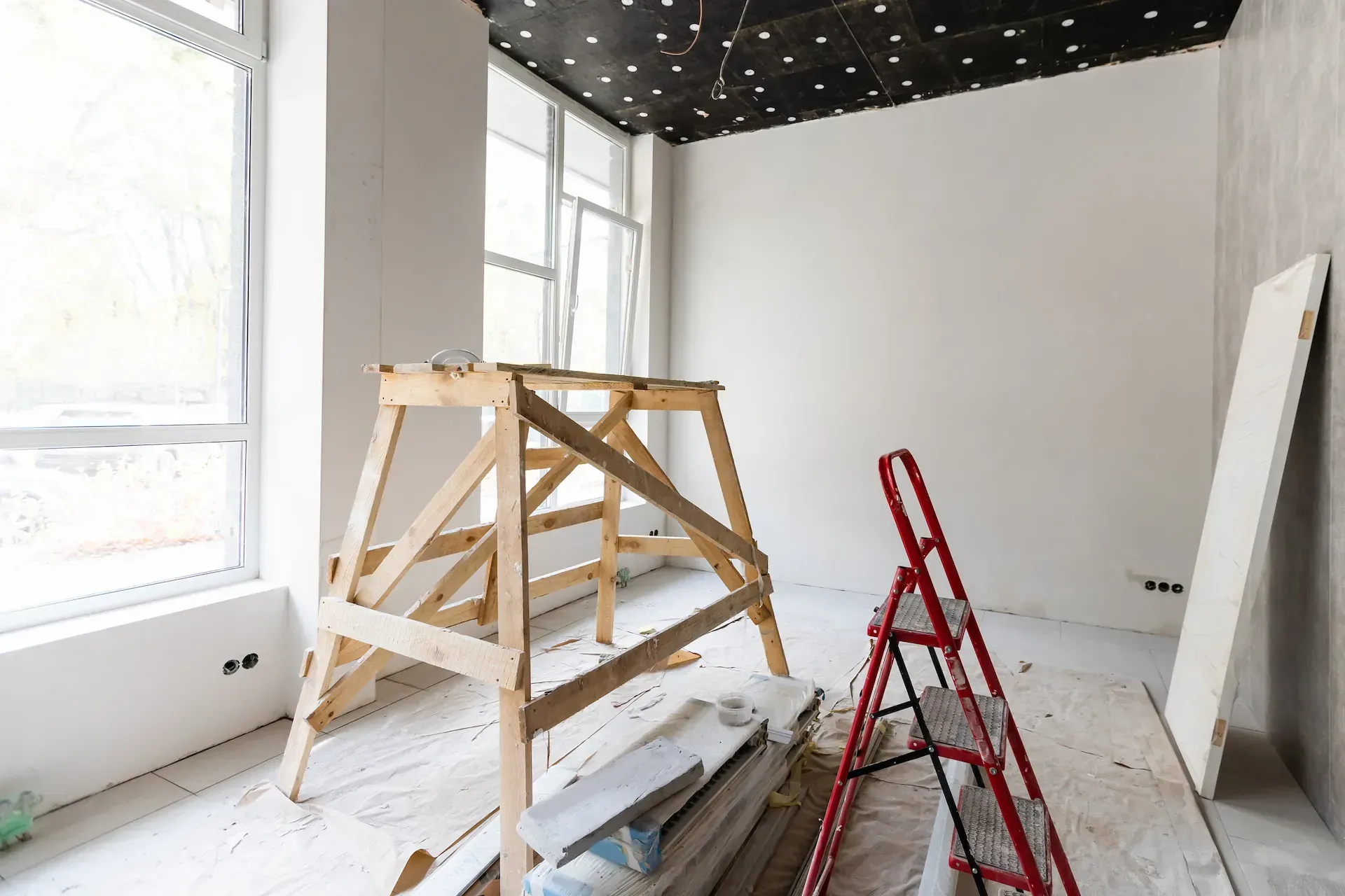 Habitación en remodelación con andamios, escalera y paneles de yeso cerca de las ventanas.