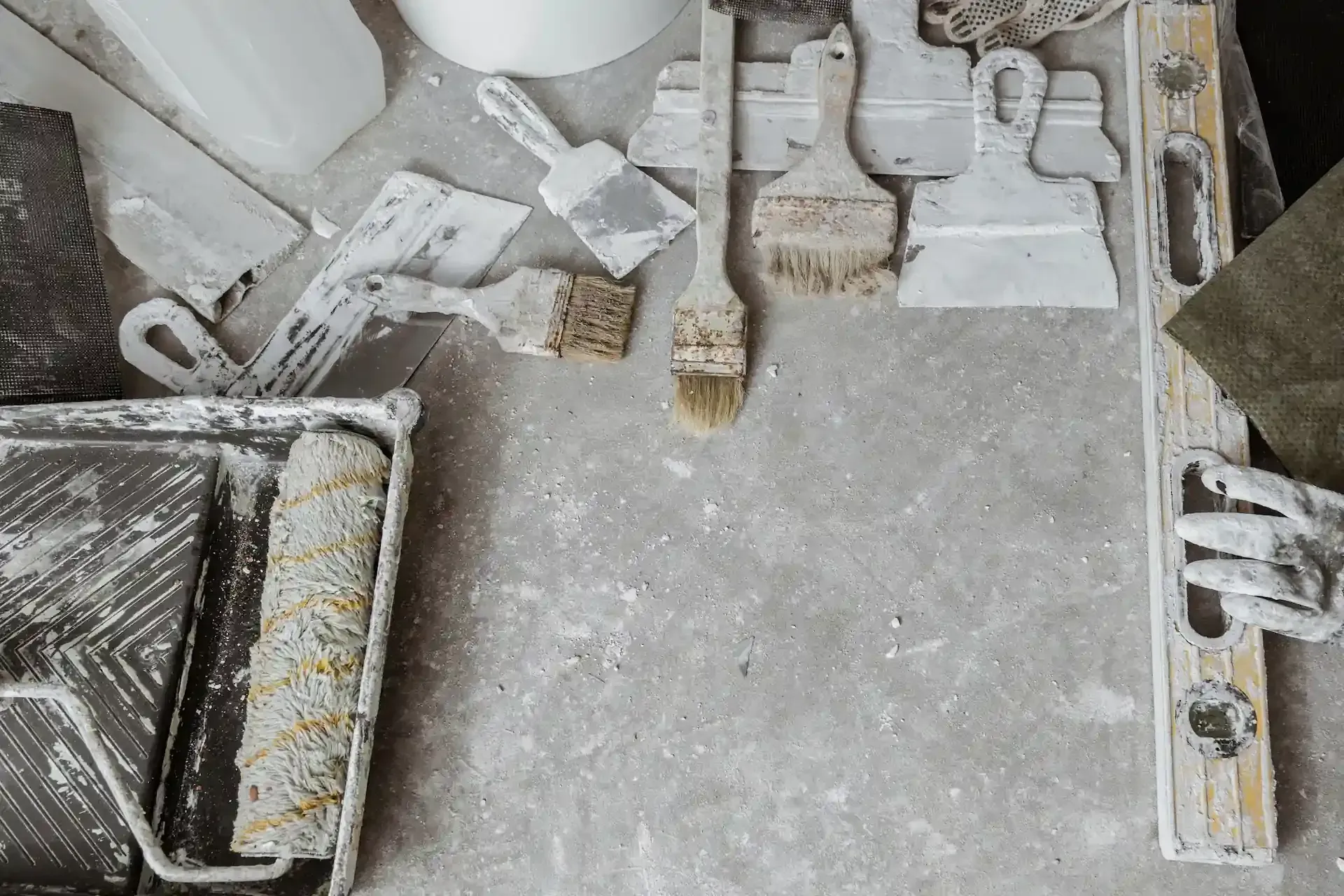 Herramientas de pintura esparcidas sobre una superficie de hormigón, incluidos rodillos, pinceles y espátulas