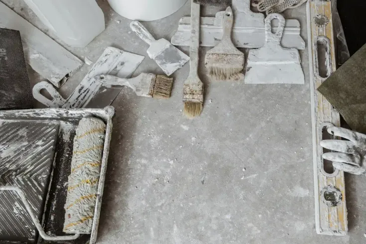 Herramientas de pintura esparcidas sobre una superficie de hormigón, incluidos rodillos, pinceles y espátulas
