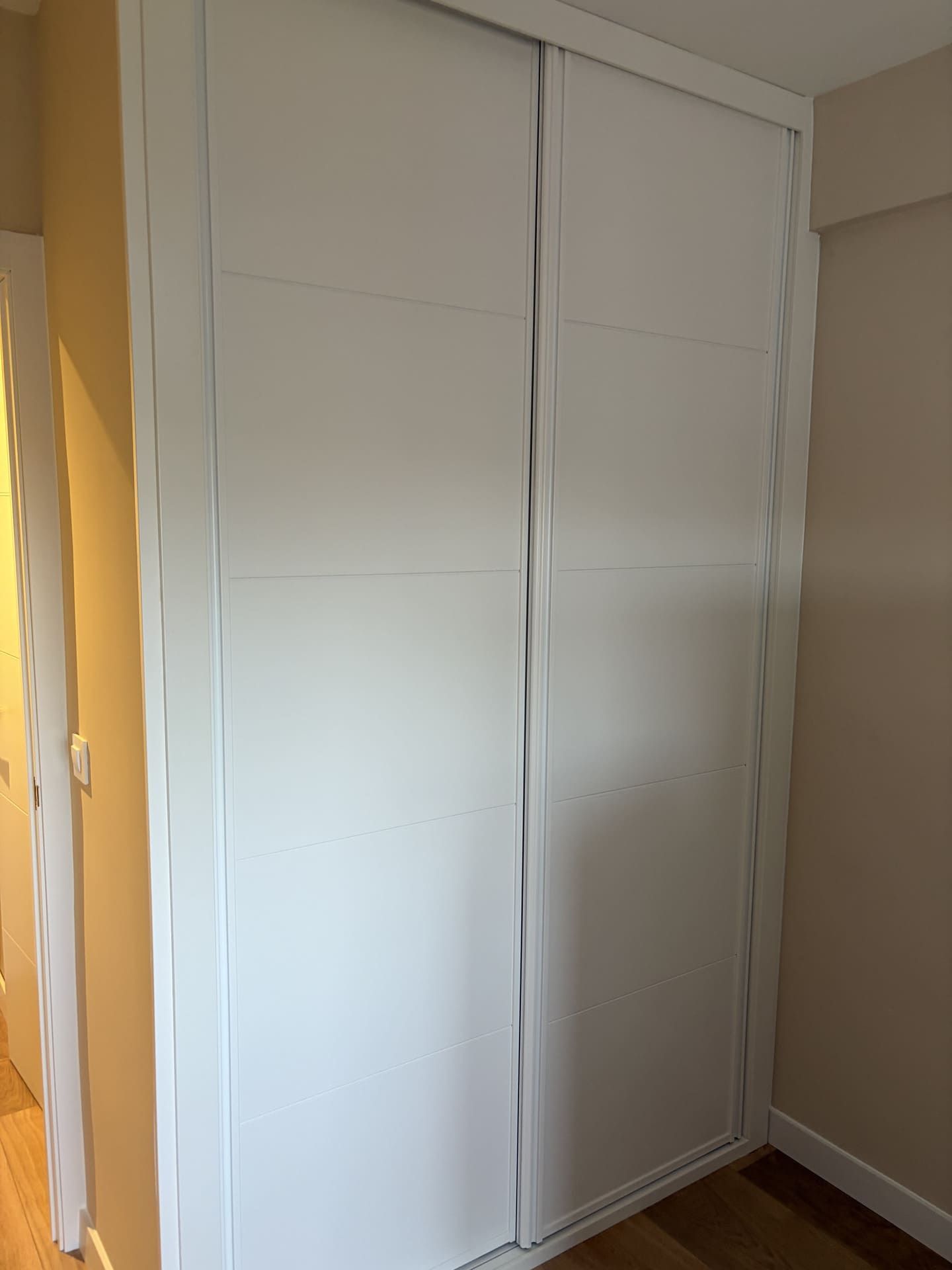 Armario con puertas corredizas de color blanco en una habitación con paredes de color claro y suelo de madera.