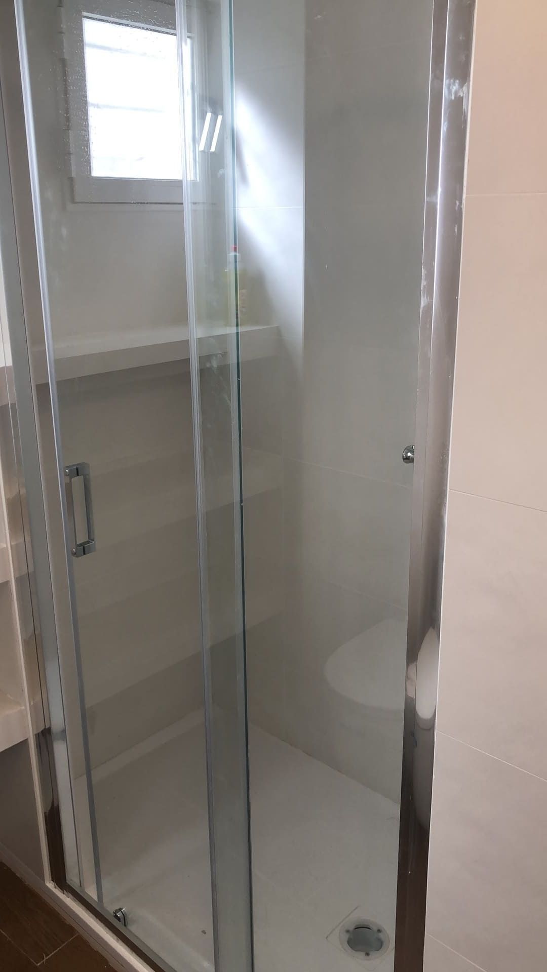 Mampara de ducha de cristal en baño con paredes blancas.