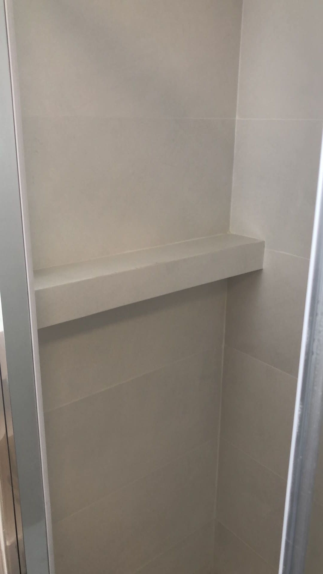 Una repisa empotrada en una ducha alicatada. La repisa es de un color neutro claro, a juego con las paredes.