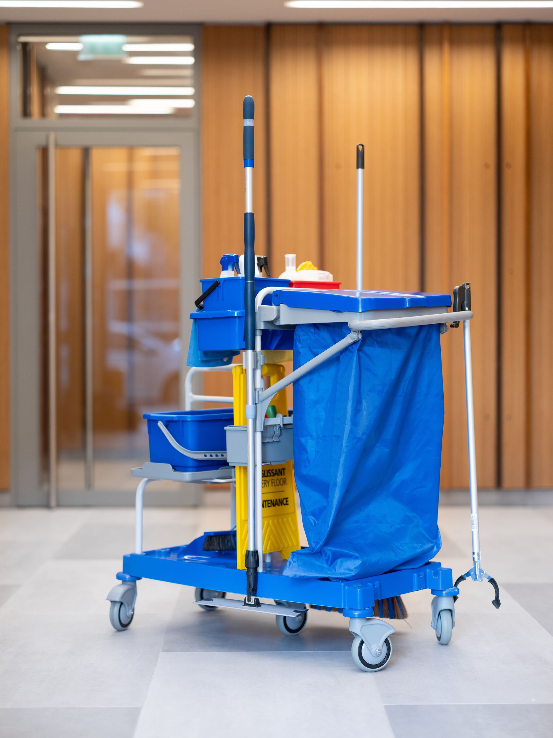 Chariot de nettoyage bleu contenant des produits de nettoyage dans un couloir.