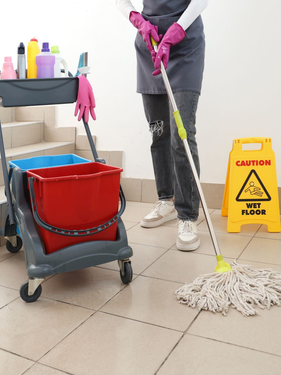 Personne passant la serpillière. Chariot de nettoyage, panneau jaune, gants roses.