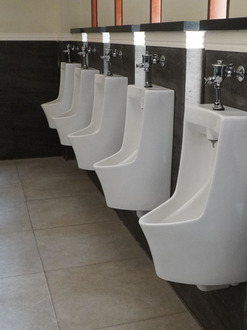 Rangée d'urinoirs blancs dans des toilettes publiques aux murs gris et marron et au sol carrelé clair.