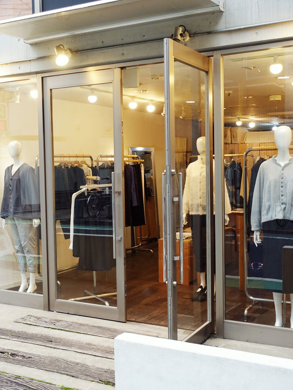 Façade de magasin avec portes vitrées, mannequins habillés, portants de vêtements.