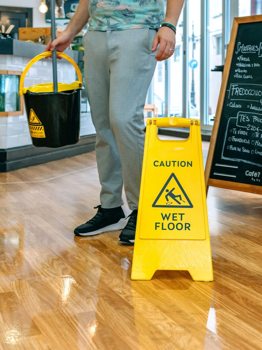 Une personne tenant un seau se tient près d'un panneau jaune sur un parquet brillant.