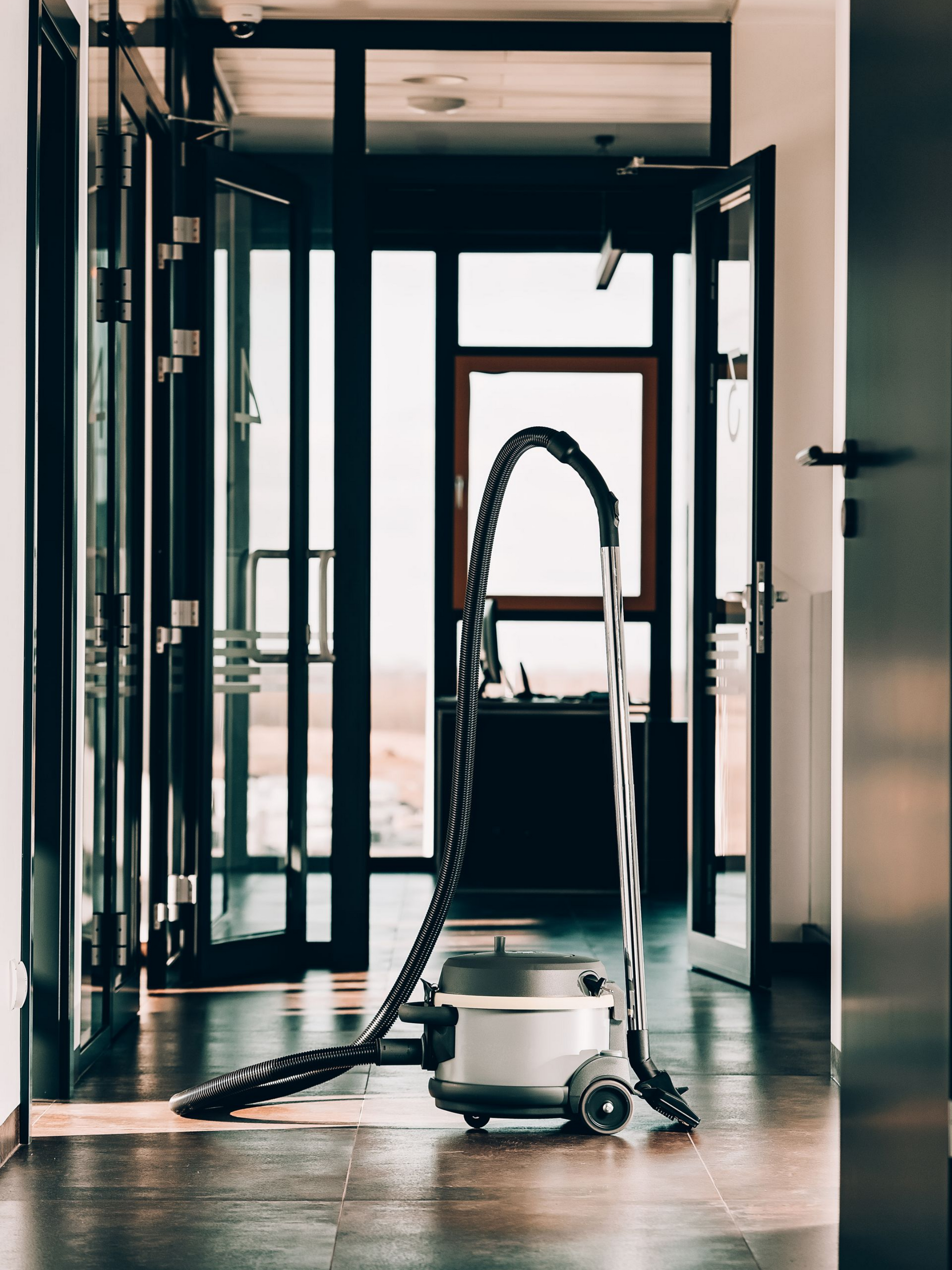Aspirateur dans le couloir, tuyau arqué. Pièce lumineuse, portes et encadrements de fenêtres sombres.