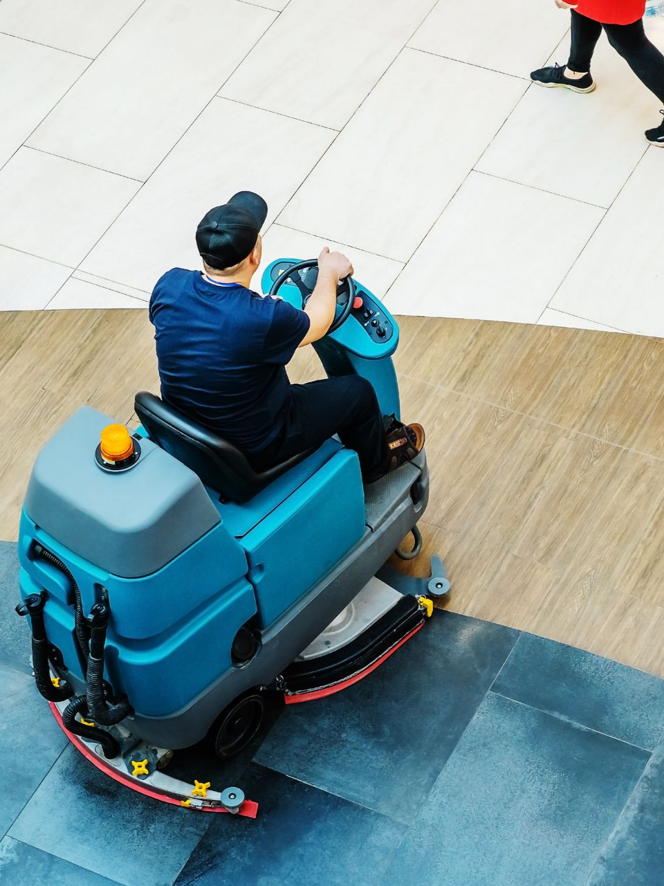 Une personne utilise une autolaveuse bleue dans un bâtiment, nettoyant un sol carrelé.