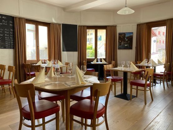 Salle à manger de restaurant vide avec tables en bois, chaises rouges et fenêtres baignées de soleil
