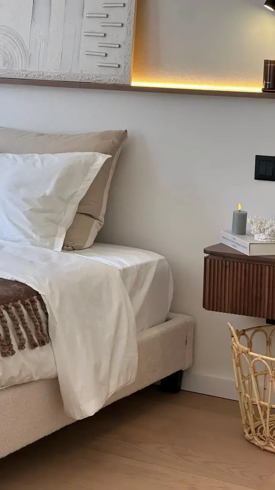 Acogedor rincón de dormitorio con cama beige, ropa de cama blanca, cuadros en la pared y una pequeña mesita auxiliar