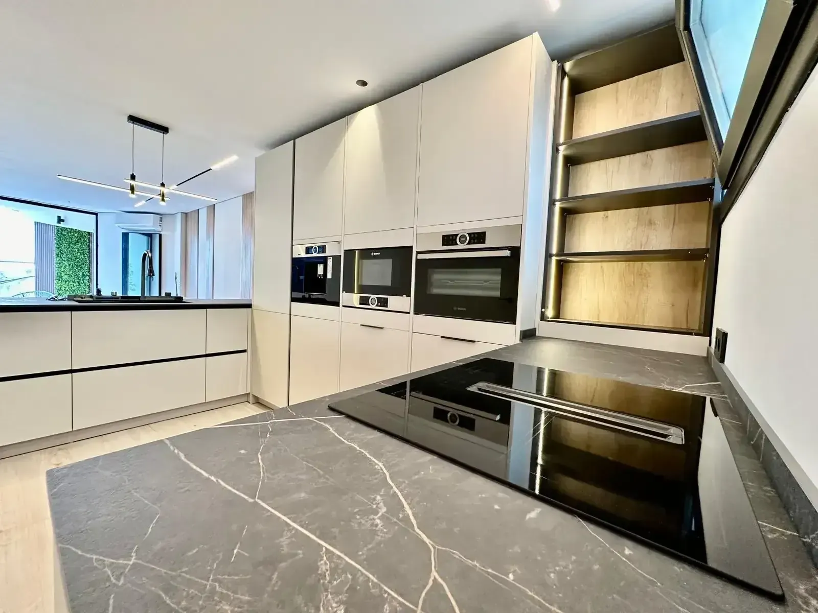 Cocina moderna blanca con isla de mármol, hornos empotrados y estanterías abiertas que dan a la zona del altillo.