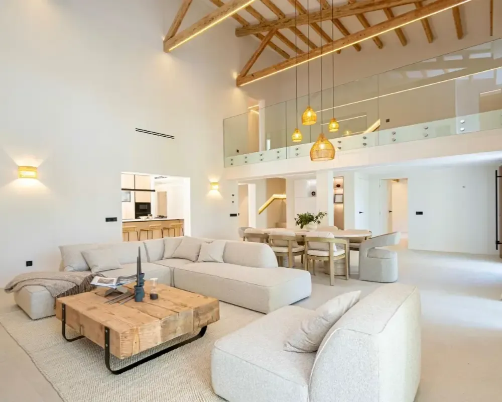 Luminoso salón moderno de planta abierta con sofás beige, mesa de centro de madera y techo abovedado alto.