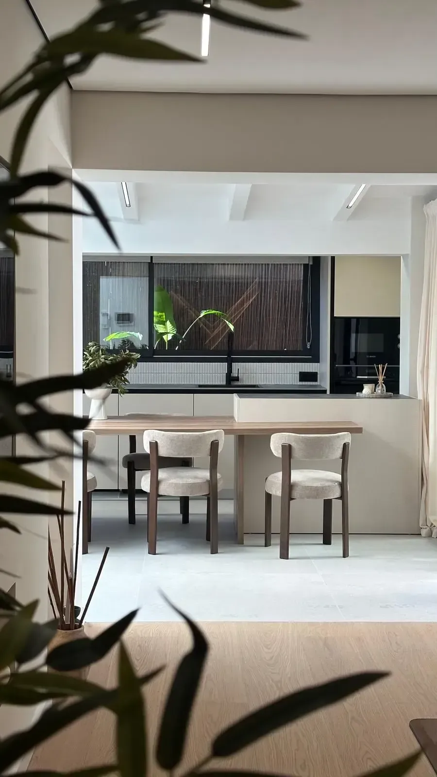 Rincón de cocina moderno con mesa, sillas y vista a la ventana, enmarcado por plantas de interior.