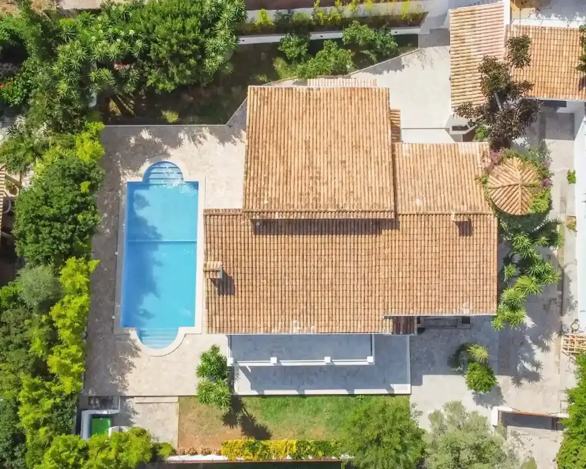 Vista aérea de una casa con techo de terracota, piscina azul y vegetación circundante.