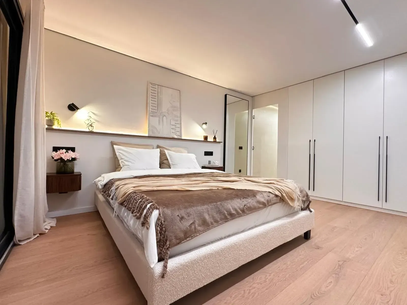 Dormitorio moderno con una cama grande, iluminación cálida y armarios blancos en un interior minimalista.