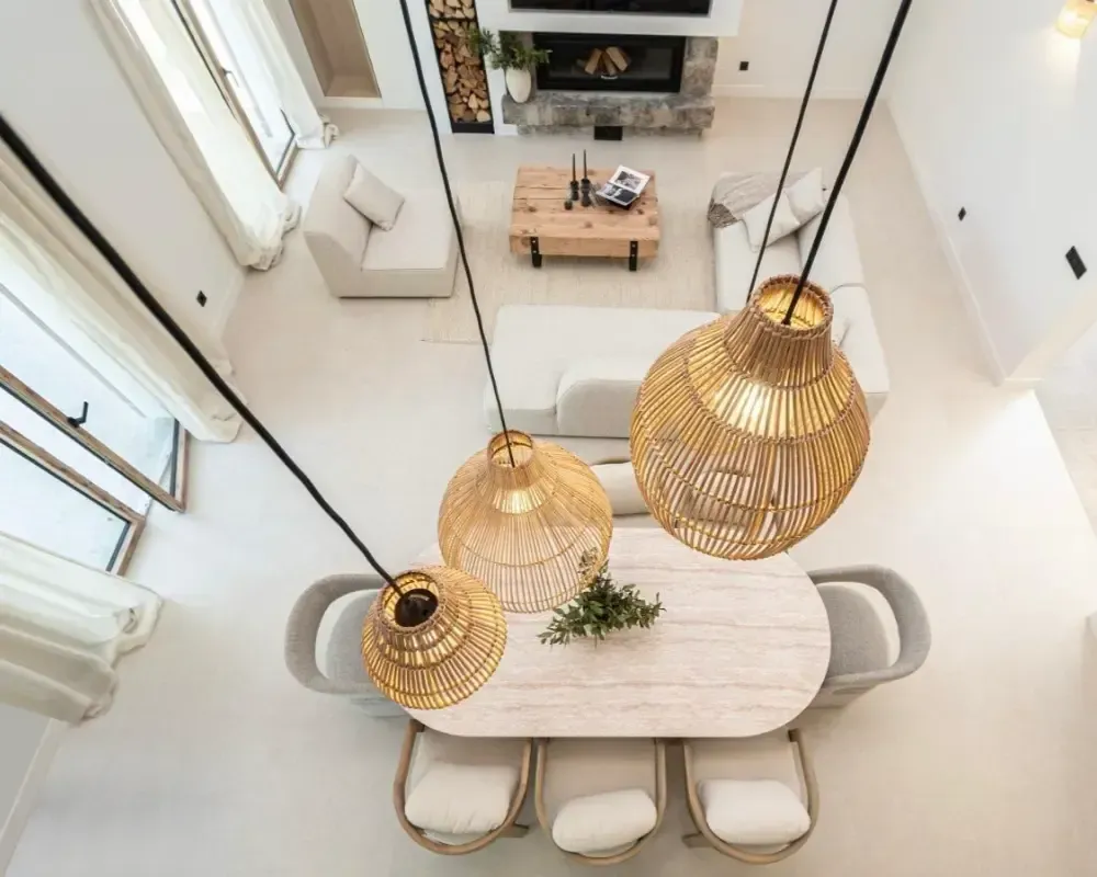 Comedor luminoso y minimalista con una mesa larga blanca, lámparas colgantes de mimbre y sillas beige.