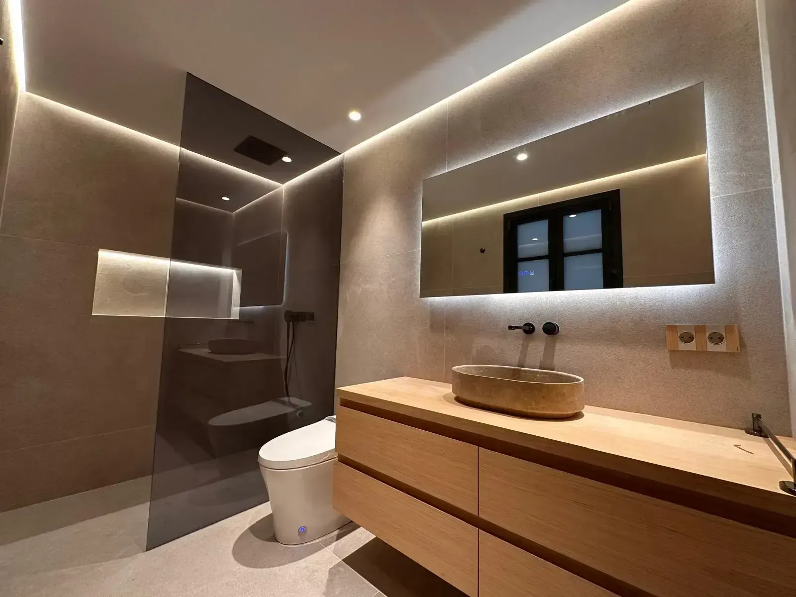 Baño moderno con ducha a ras de suelo, tocador flotante de madera y espejo con iluminación LED sobre el lavabo.