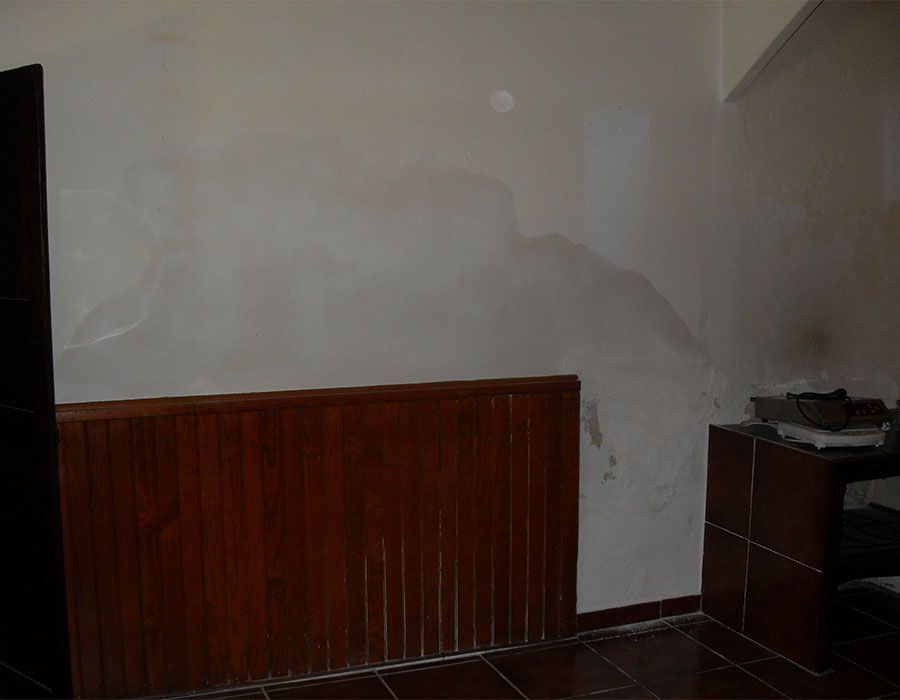Pièce dépouillée avec des murs blancs, des lambris en bois foncé et une petite commode dans un coin.